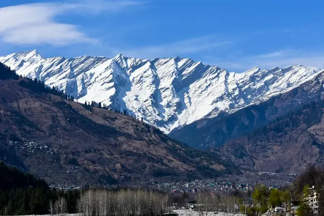 a snowy mountain range with trees and houses of Manali
